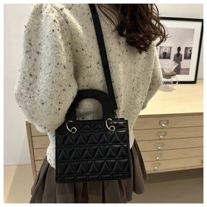 Close-up of quilted black crossbody bag featuring triangle stitching and gold metal hardware