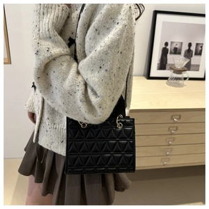 Detail of black quilted handbag with gold metal handle and triangular pattern