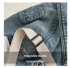 Detail of black plastic adjustment buckle on beige woven strap of denim crossbody bag