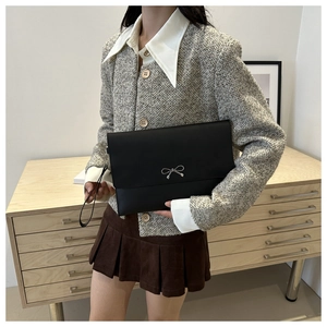 Detail of black leather envelope clutch featuring a silver metal bow and wristlet strap