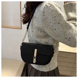 Detail of a black pebbled leather saddle bag with a sleek gold metal bar and chain strap