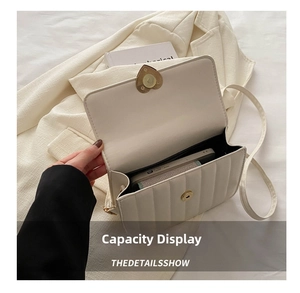 Capacity view of white quilted shoulder bag with gold heart clasp holding a smartphone