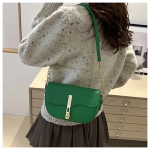 Detail view of a bright green saddle crossbody bag with a gold buckle on a model