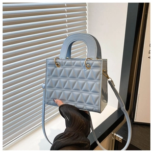 Detail of light blue quilted handbag featuring geometric triangle stitching and gold metal rings