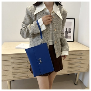 Royal blue slim envelope clutch bag with silver bow detail held by model in office setting