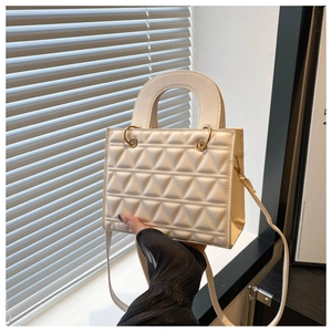 Close-up of beige quilted handbag featuring triangular stitching and gold ring hardware