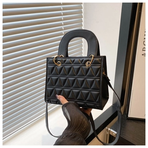 Detail of black geometric quilted handbag with golden metal hardware and top handle