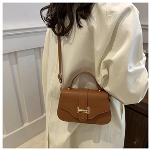Detail of caramel brown crossbody bag with gold hardware worn over a white coat