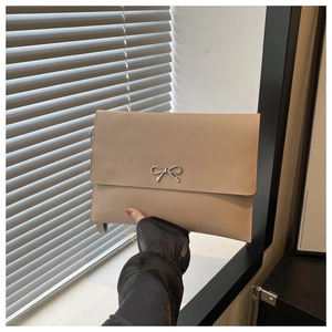 Detail of beige envelope clutch bag featuring a silver metal bow and thin strap texture