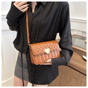 Detail of caramel quilted crossbody bag with golden heart-shaped clasp and leather strap
