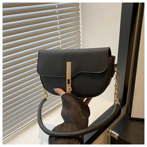 Detail of black lychee grain leather saddle bag featuring modern gold metal bar buckle