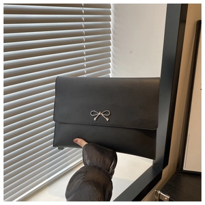 Detail shot of a black envelope clutch featuring a decorative silver metal bow clasp