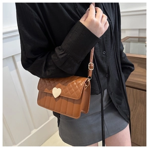 Detail of quilted brown crossbody bag featuring a golden heart-shaped metal buckle clasp