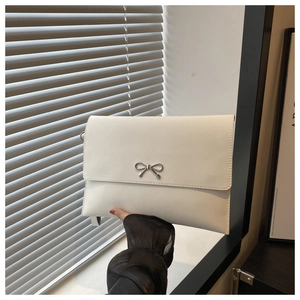 Close-up of a white envelope clutch bag featuring a silver metal bow clasp and smooth texture