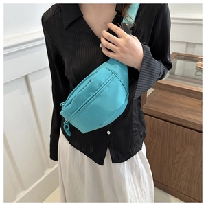 Adjustable blue nylon crossbody chest bag shown on model with striped shirt and white skirt