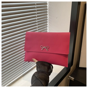Macro shot of rose red envelope clutch featuring a sleek silver metal bow decoration