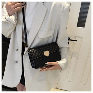 Close-up of black quilted shoulder bag featuring a gold heart clasp and mixed textures