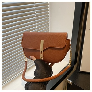 Detail of tan lychee pattern saddle bag featuring a long gold metal buckle and chain strap