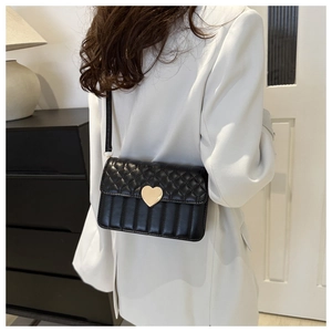 Detail of black quilted crossbody bag with gold heart clasp and white suit styling
