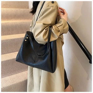 Détail du grand cabas en cuir noir avec rivets métalliques porté sur un trench-coat beige