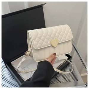 Detail of quilted crossbody bag featuring a golden heart-shaped clasp and ivory leather texture