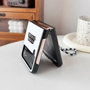 Detail of Galaxy Z Flip4 case with checkered wrist strap and retro emblem on wooden desk