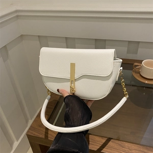 Elegant white saddle bag with golden clasp and leather strap in minimalist interior