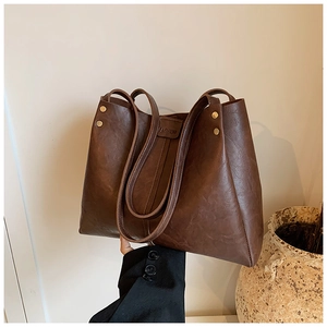 Détail du sac cabas en cuir marron foncé avec rivets dorés et étiquette gaufrée