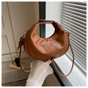 Détail d'un sac à main demi-lune caramel tenu sous une douce lumière de fenêtre