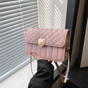 Pink quilted shoulder bag with golden heart buckle held against a natural light window