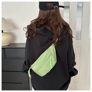 Detail view of a green casual chest bag with woven zipper pulls worn by a model