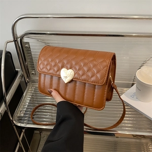 Brown quilted crossbody bag with heart-shaped lock on a modern minimalist shelf