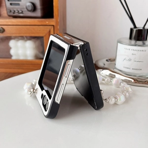 Detail of folding phone case with pearl and laser bead hand strap on marble surface