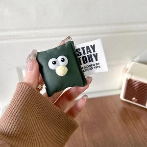 Close-up of cute plush green pillow phone grip with big eyes and a branded textile label