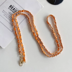 Detail of gold metal chain woven with orange leather strap and lobster clasps