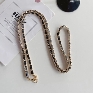 Macro shot of gold metal chain woven with black leather strap and lobster clasp detail