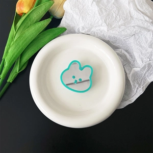Close-up of a bear-shaped portable makeup mirror with a green frame on a white plate