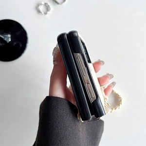 Detail view of foldable phone case side cutouts and gold metal chain strap on white desk