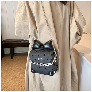 Detail of grey polka dot crossbody bag with black bow and dual silver chain straps