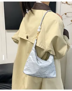 Detail of grey pleated shoulder bag with large pearl accents worn with a beige trench coat