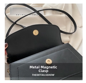Detailed close-up of a matte gold magnetic buckle on a black textured leather handbag