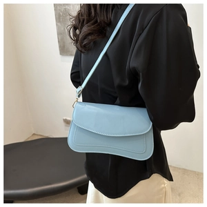 Detail of light blue minimalist leather shoulder bag worn over a black stylish outfit