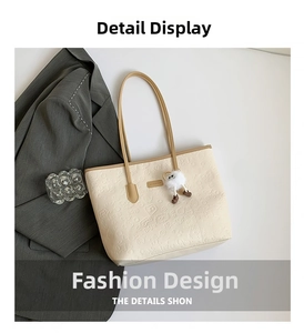 Detail view of large cream tote bag featuring embossed cartoon patterns and plush charm