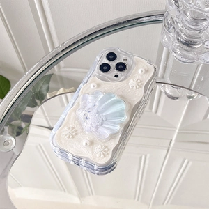 Detail of iPhone case featuring large shell decoration and pearls on a glass surface