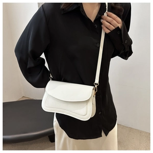 Close-up of white crossbody bag with wavy flap and metal twist lock on a black shirt