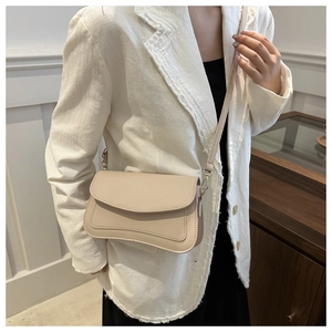 Detail of beige PU leather small square bag with curved stitching on a white blazer