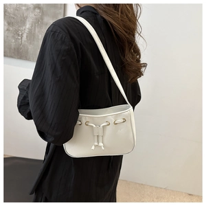 Model wearing a white patent leather underarm bag with drawstring and gold eyelets
