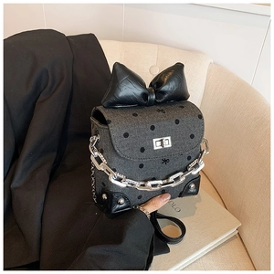 Detail of grey herringbone crossbody bag with polka dots and oversized black bow