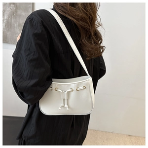 White minimalist drawstring baguette bag with gold grommets shown on model's shoulder