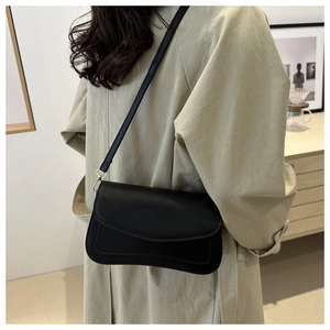 Detail of a black matte crossbody bag with curved flap and leather strap worn by a model